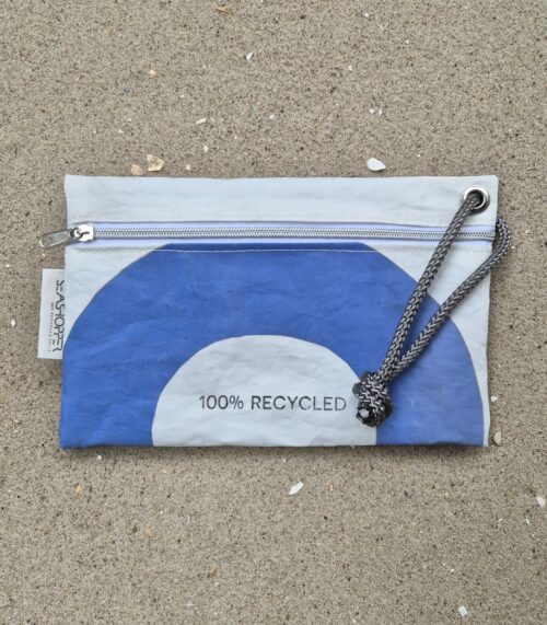 Biała saszetka z żagla z recyclingu leżąca na piasku.